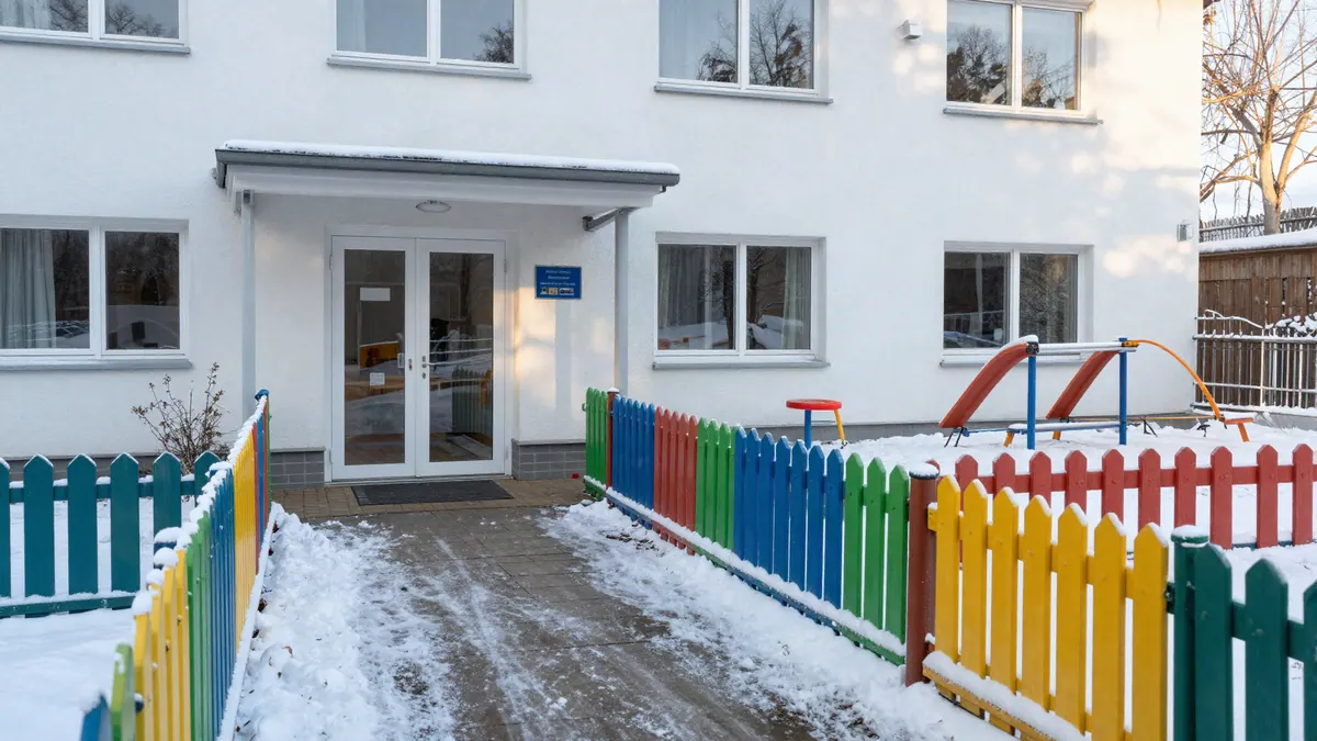 Geräumter Zuweg zum Eingang einer Kita mit verschneitem Spielplatz